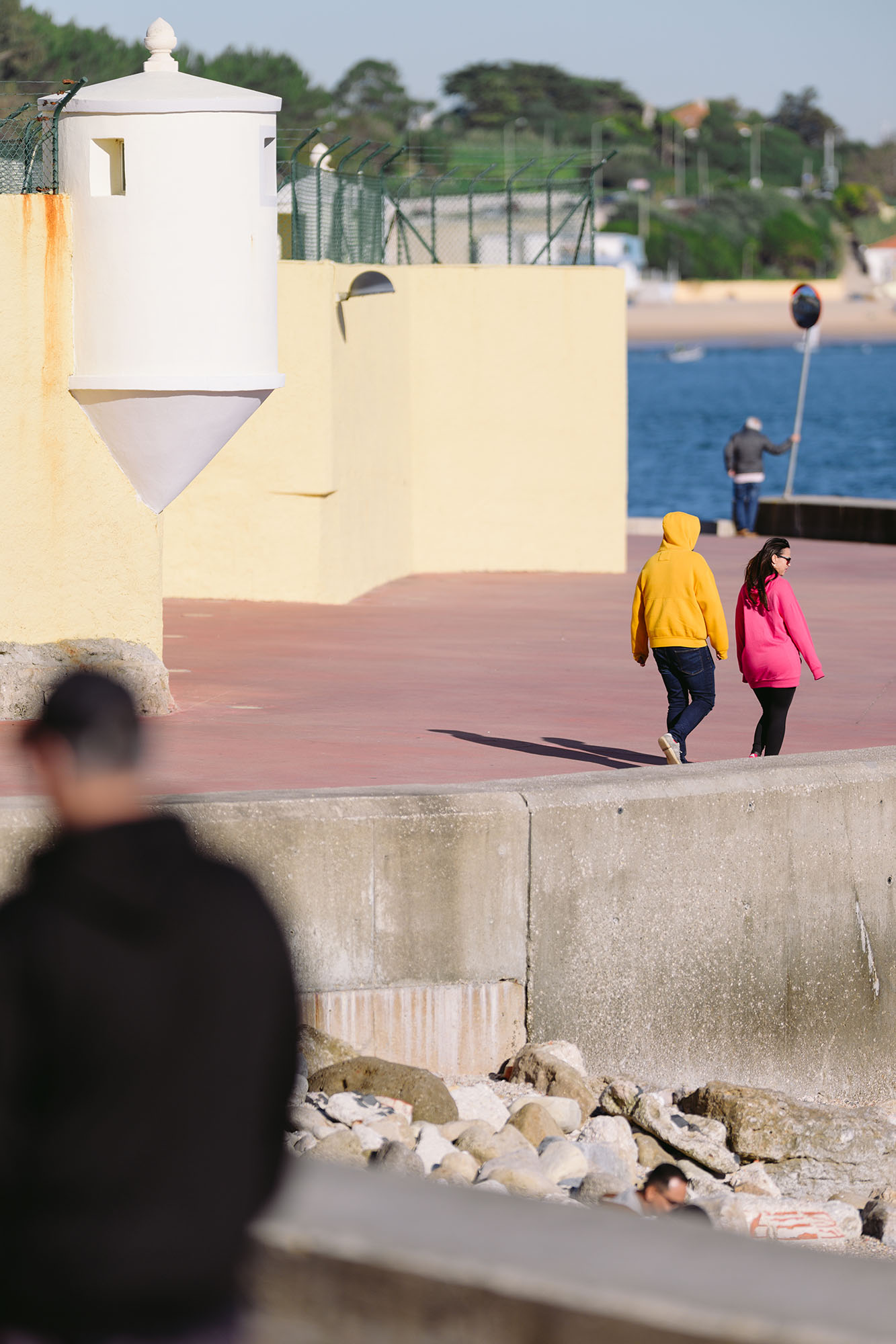 Couple in yellow and pink sweaters walking along the coast in Oeiras, Portugal